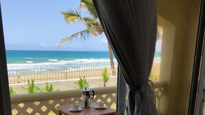 A balcony with a view of the beach and ocean, a table with a coffee pot, and two chairs. - Barefoot Beach Pad (Cabarete)
