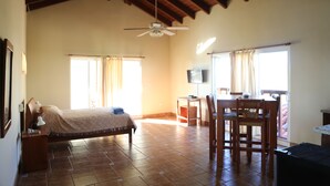 A spacious room with a bed, a desk, and a chair. There is a ceiling fan and a window with curtains. - Barefoot Beach Pad (Cabarete)