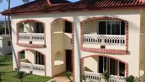 A multi-story building with balconies, a tiled roof, and a well-maintained lawn. - Barefoot Beach Pad (Cabarete)