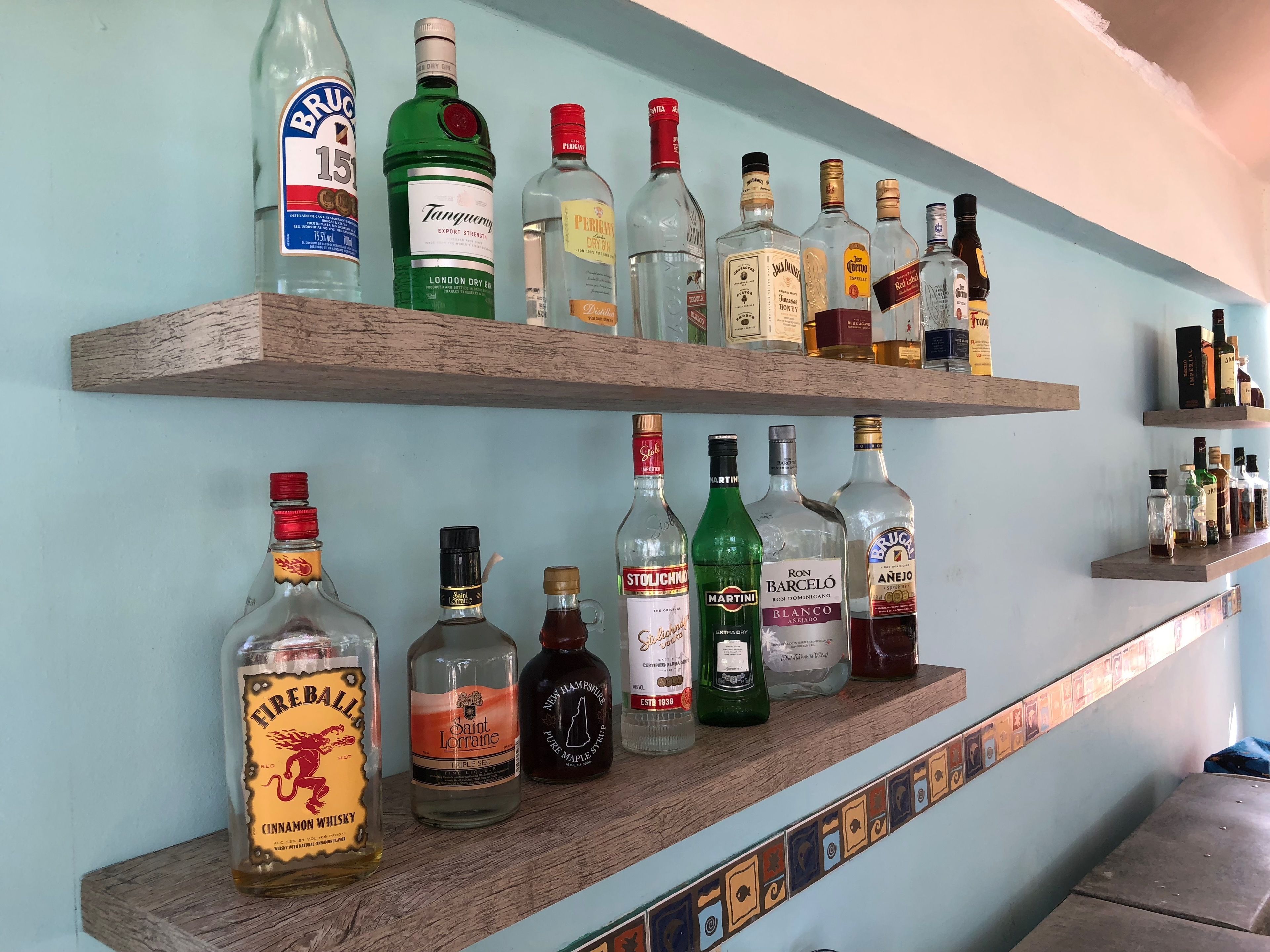 Una pared con dos estantes de madera que exhiben varias botellas de alcohol.