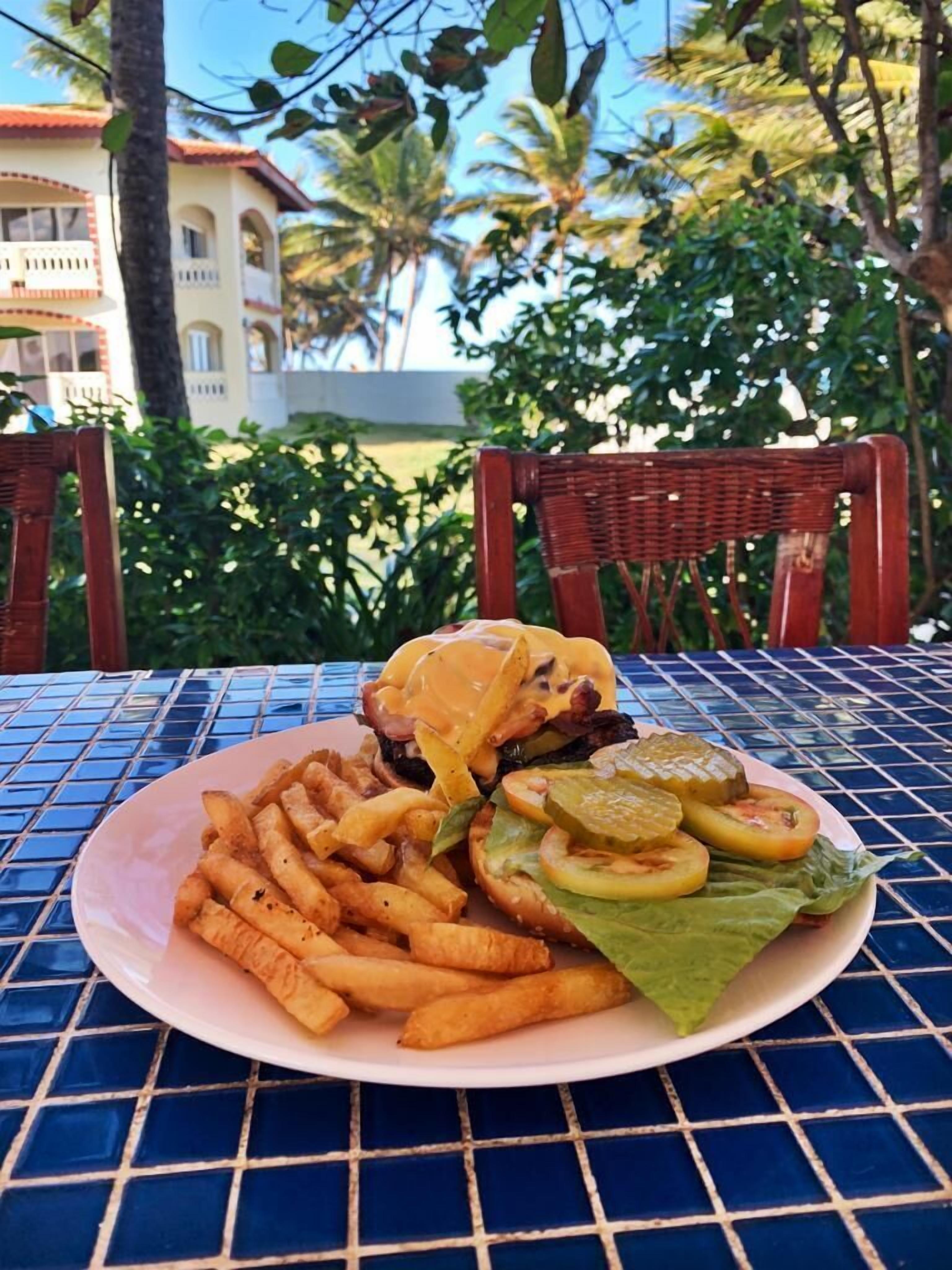 Un plato de comida con una hamburguesa, papas fritas y pepinillos sobre una mesa con superficie de azulejos azules.