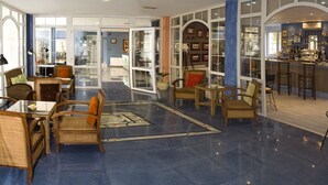 Un vestíbulo espacioso con una zona de bar, diferentes disposiciones de asientos y una entrada con puerta de cristal.