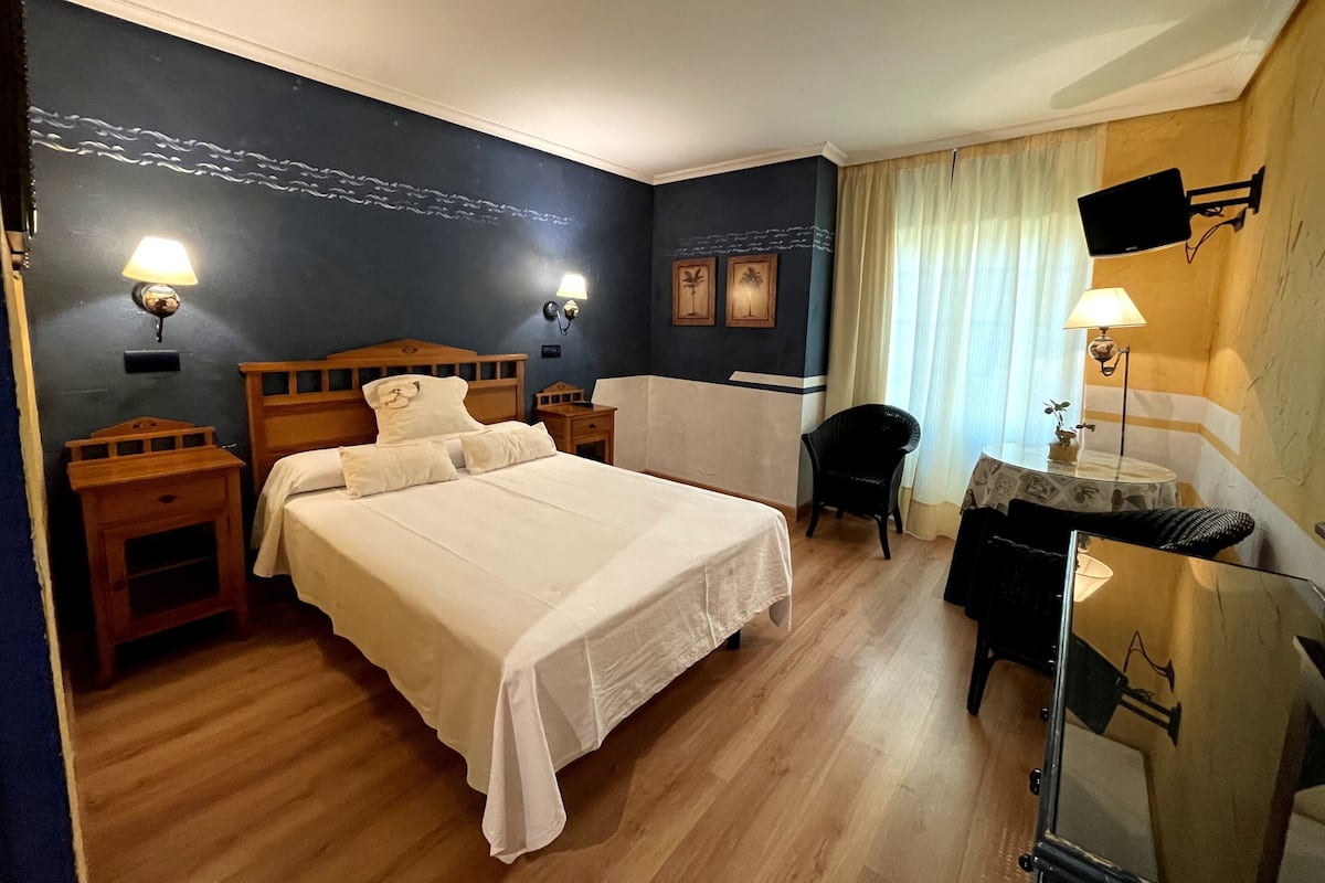Habitación de hotel con una cama grande, dos mesitas de noche, un escritorio con una silla, un televisor y una ventana con cortinas.
