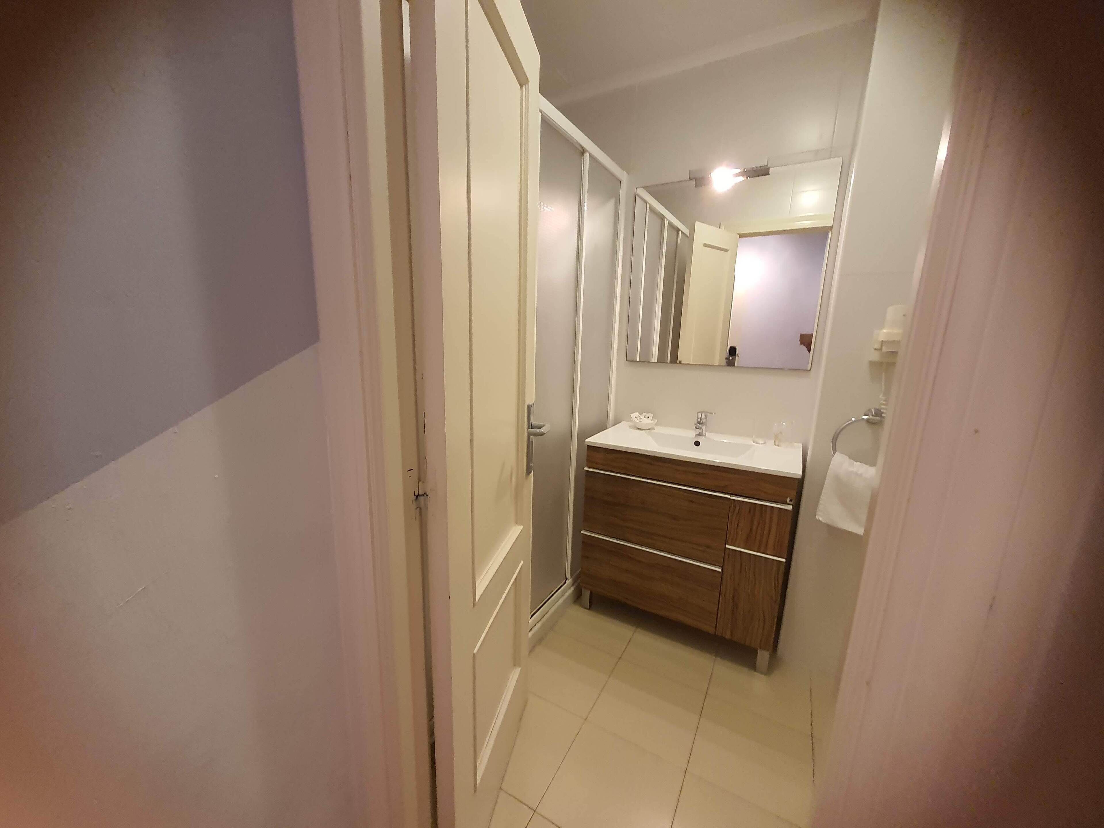 Un pasillo estrecho que conduce a un baño con lavamanos, espejo y toallero.