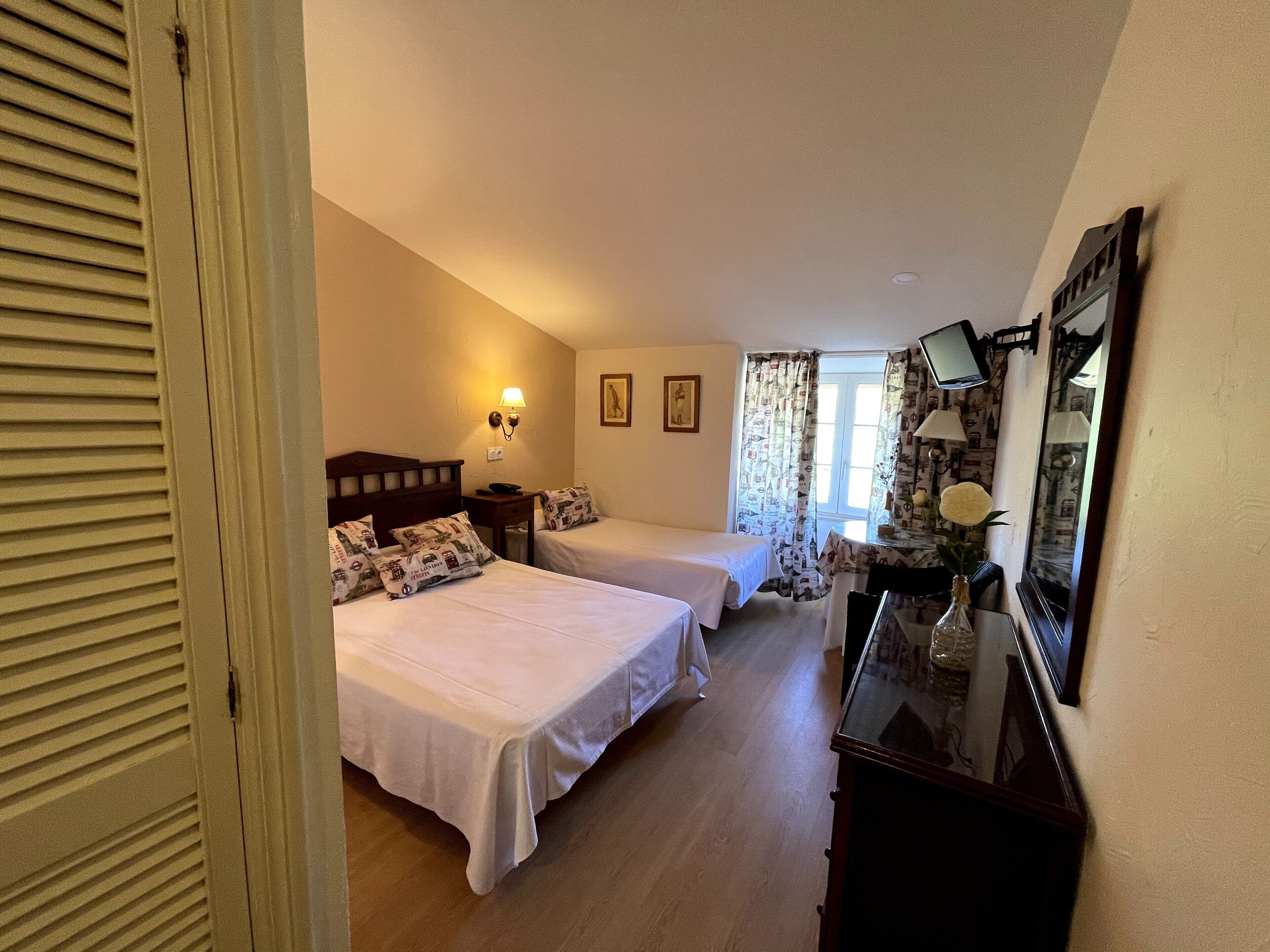 Habitación de hotel con dos camas, un escritorio, una silla, un espejo y una ventana con cortinas.