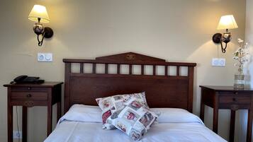 Una cama bien hecha con un cojín estampado, dos mesitas de noche con lámparas y un enchufe de pared.