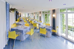 Un comedor amplio con mesas dispuestas para varios comensales, grandes ventanales que aportan luz natural y un diseño de interiores moderno.