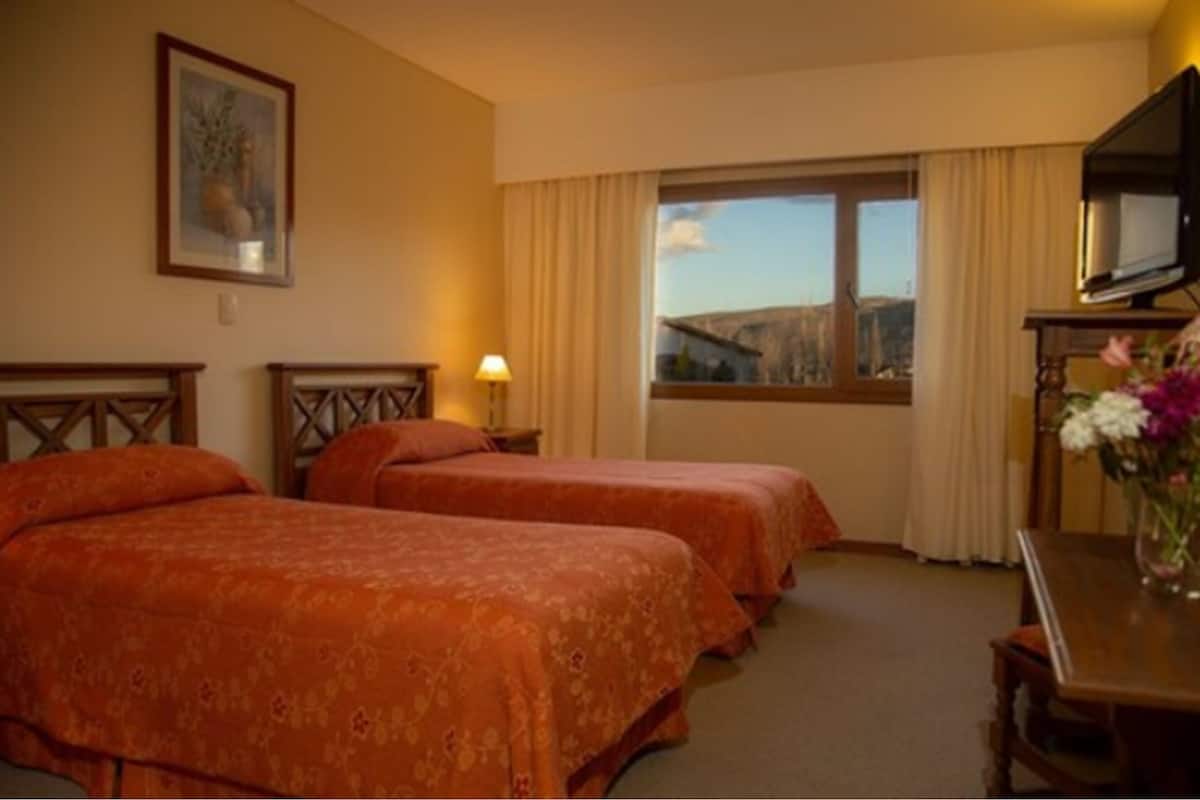 A hotel room with two beds, a television, and a window with a view of the outdoors.