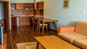 A compact living space with a wooden dining table, chairs, a sofa, and a kitchenette. - Evergreen Aparthotel & Spa (Bansko)