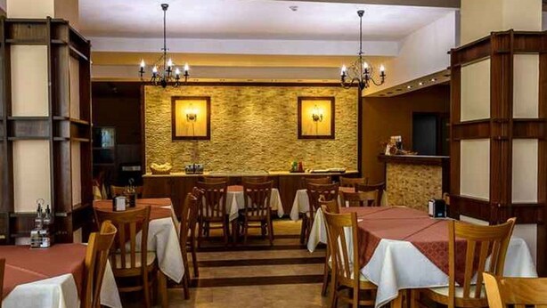 A restaurant with wooden tables and chairs, a stone wall with two illuminated signs, and a bar area with a counter and stools. - Evergreen Aparthotel & Spa (Bansko)