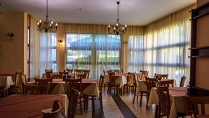 A dining area with multiple tables and chairs, large windows with curtains, and chandeliers. - Evergreen Aparthotel & Spa (Bansko)