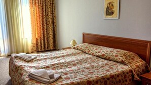 A hotel room with a bed, floral bedspread, a nightstand with a lamp, and a wall-mounted artwork. - Evergreen Aparthotel & Spa (Bansko)