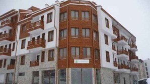 A multi-story building with balconies and large windows, surrounded by snow. - Evergreen Aparthotel & Spa (Bansko)