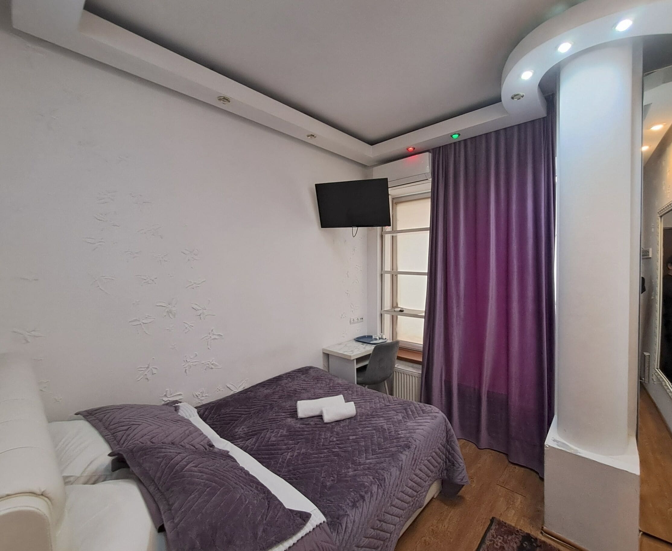 A bedroom with two beds, a TV, a window with curtains, and a small desk.