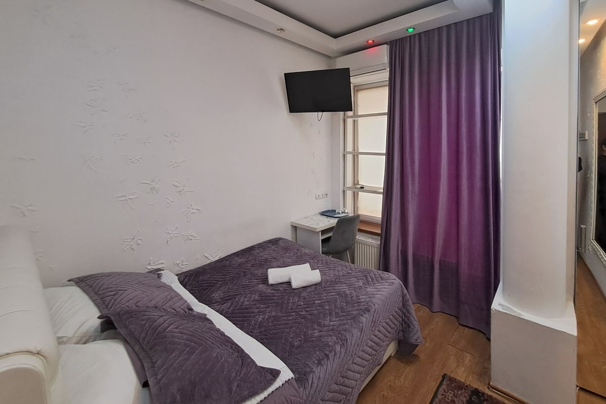 Un dormitorio con dos camas, televisión, ventana con cortinas y un escritorio pequeño.