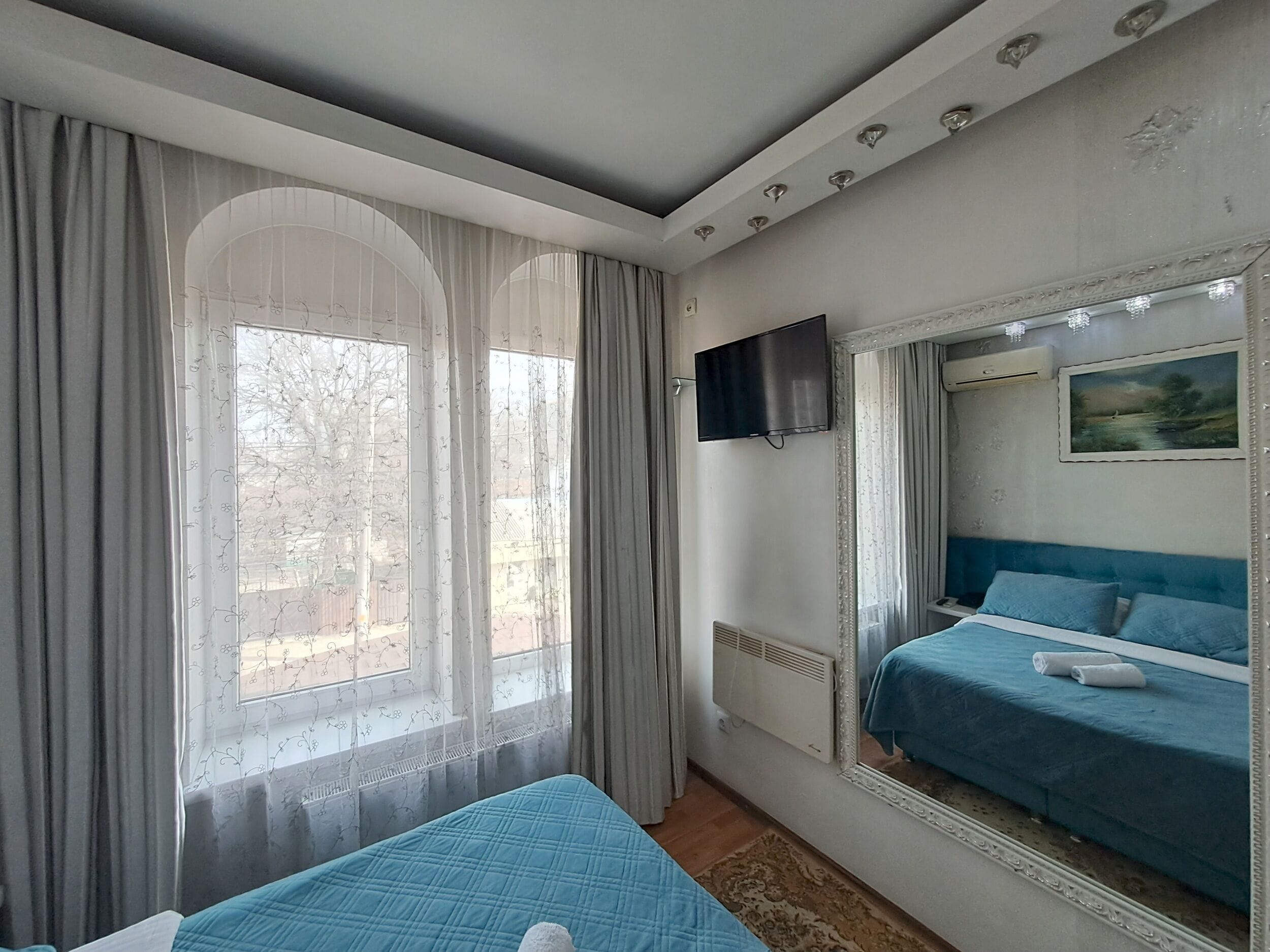 A bedroom with a bed, a TV, a window with curtains, and a painting on the wall.