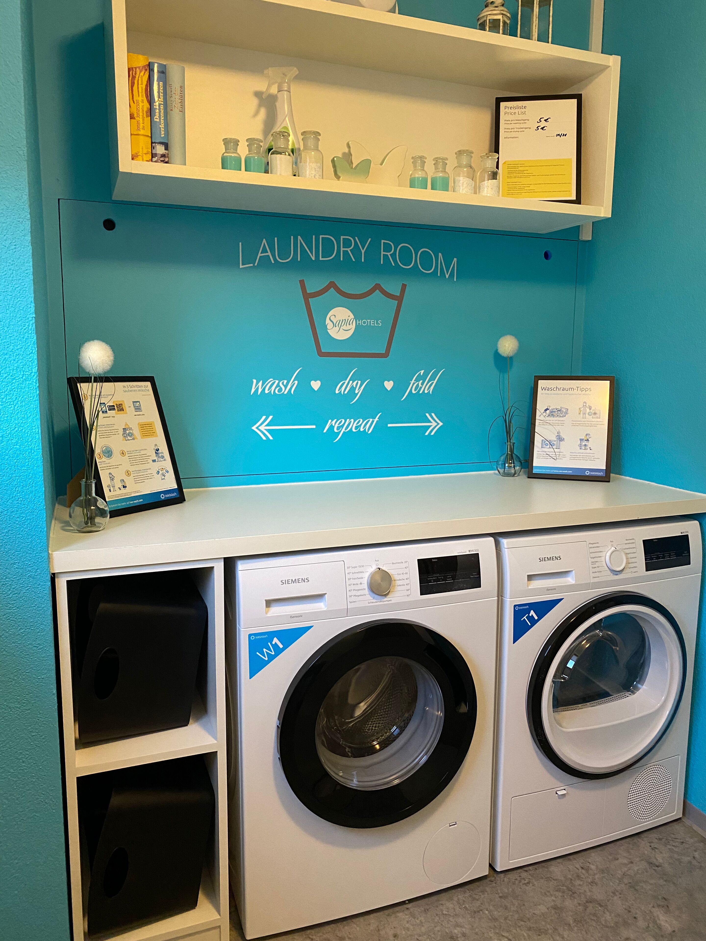 A laundry room with two Siemens T1 front-loading washing machines, a shelf with cleaning supplies, and a wall sign with washing instructions.