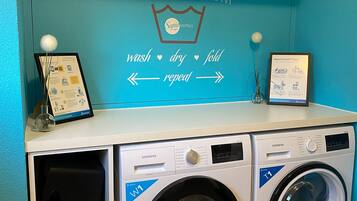 A laundry room with two Siemens T1 front-loading washing machines, a shelf with cleaning supplies, and a wall sign with washing instructions.