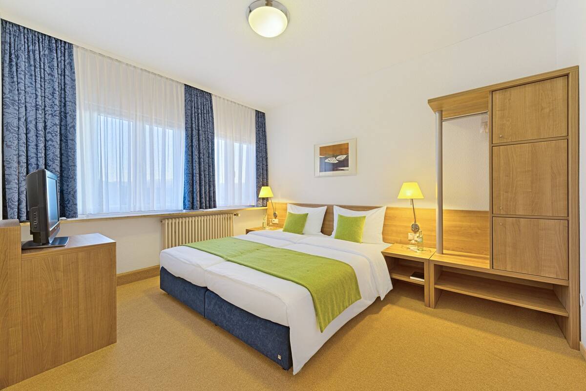 A hotel room with a bed, bedside lamps, a wardrobe, and a television on a stand.