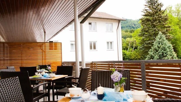 An outdoor dining area with tables and chairs, a wooden pergola, and a view of a building and trees. - St. Fridolin (Bad Saeckingen)