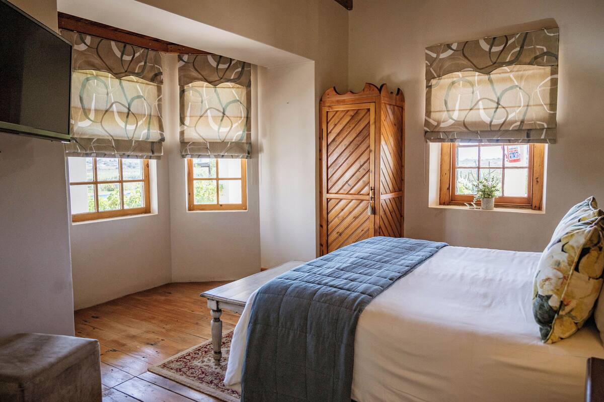 Un dormitorio con cama, un armario de madera y dos ventanas con cortinas.