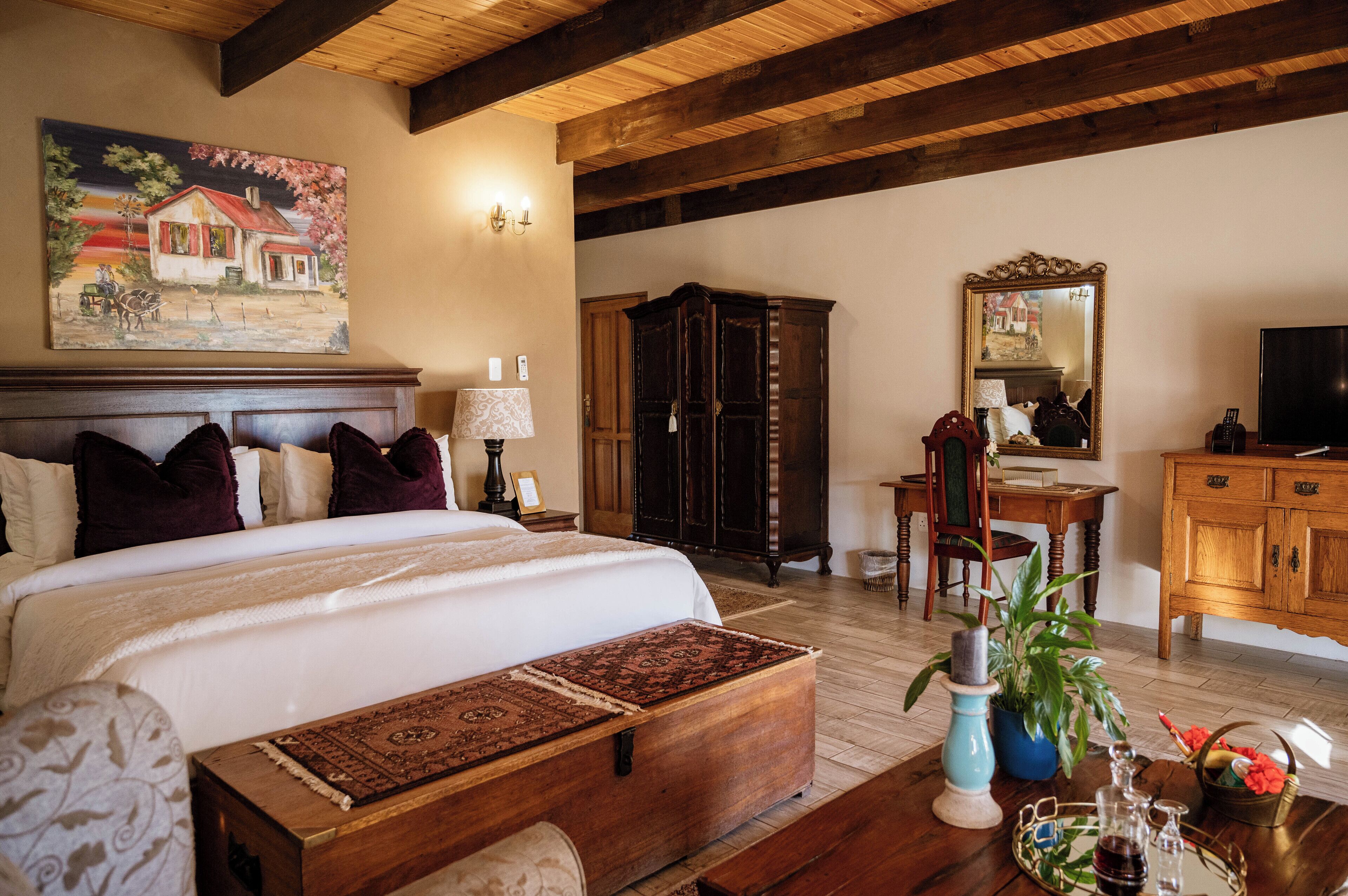 A bedroom with a large bed, wooden headboard, a nightstand with a lamp, a dresser, a mirror, and a television.