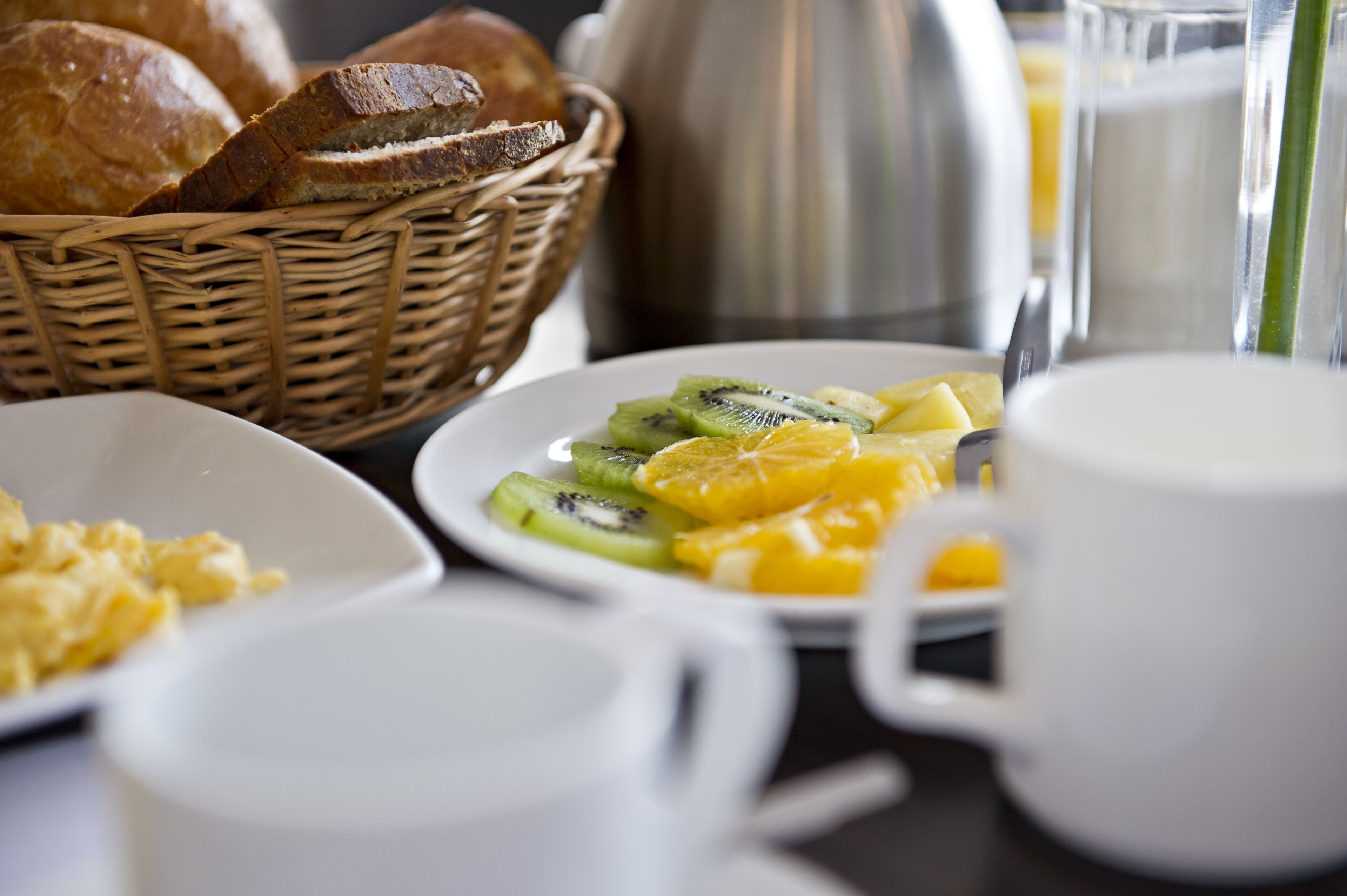 Una mesa de desayuno con una fuente de fruta, una taza y una cesta de pan.