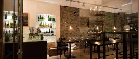Un área de bar moderna con estantes llenos de botellas, una pared de piedra y luces colgantes.