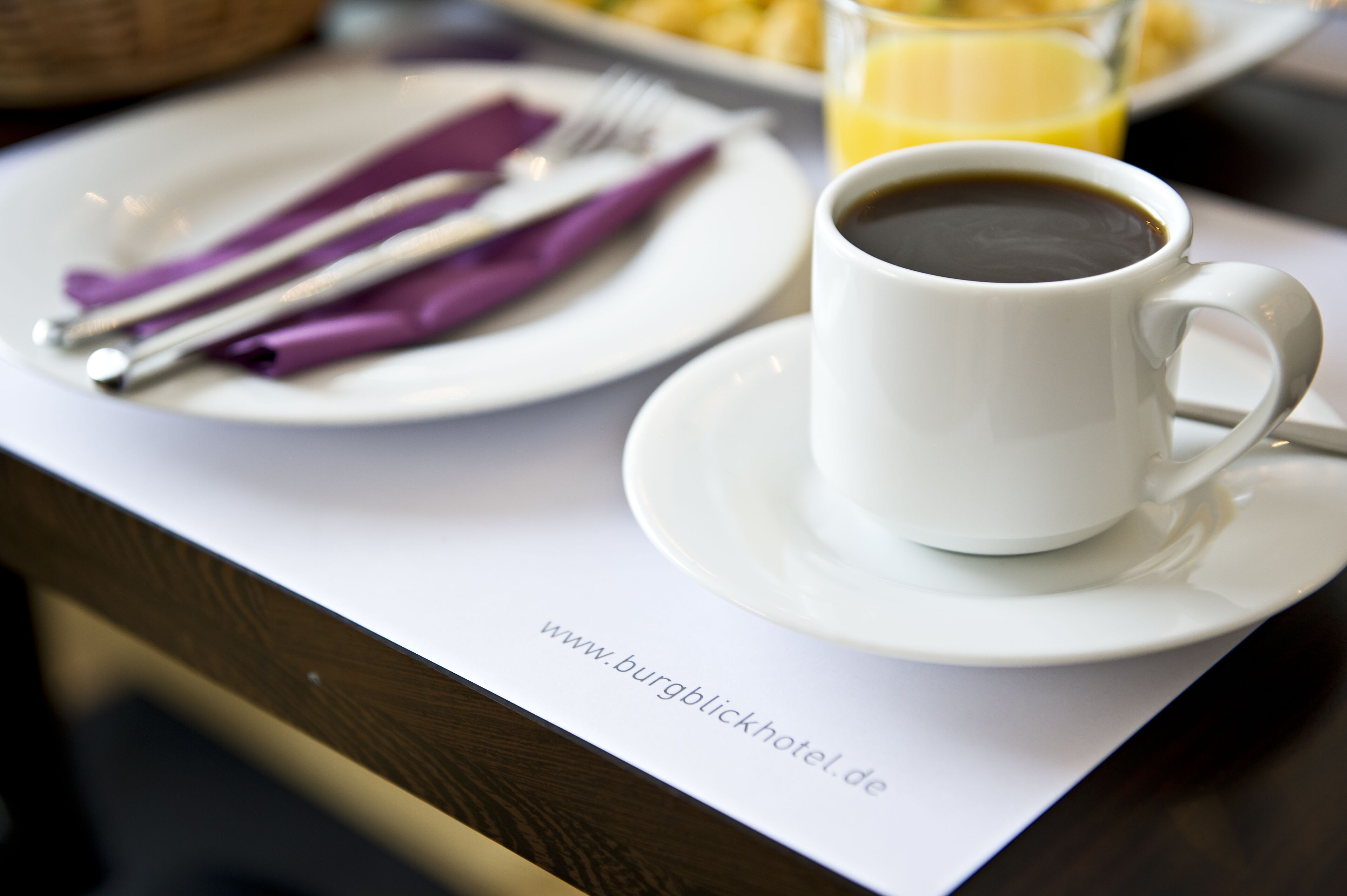 Ein Frühstückstisch mit einer Tasse Kaffee, einem Teller mit Besteck und einem Glas Orangensaft.