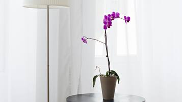 Un dormitorio con una cama, una mesa redonda con una orquídea en maceta y una lámpara de pie.