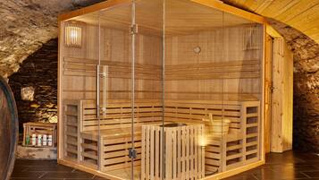 Un sauna doté de bancs en bois et de murs en verre, aménagé dans une pièce aux murs de pierre et au plafond en bois.