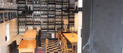 A restaurant with a checkered floor, wooden tables, and chairs. There are shelves with bottles of wine in the background.