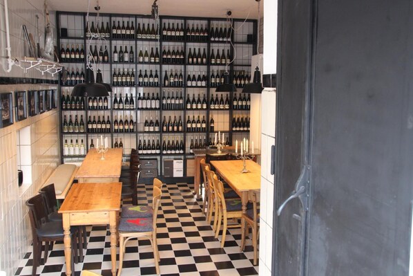Un restaurante con piso a cuadros, mesas y sillas de madera. En el fondo, hay estantes con botellas de vino.