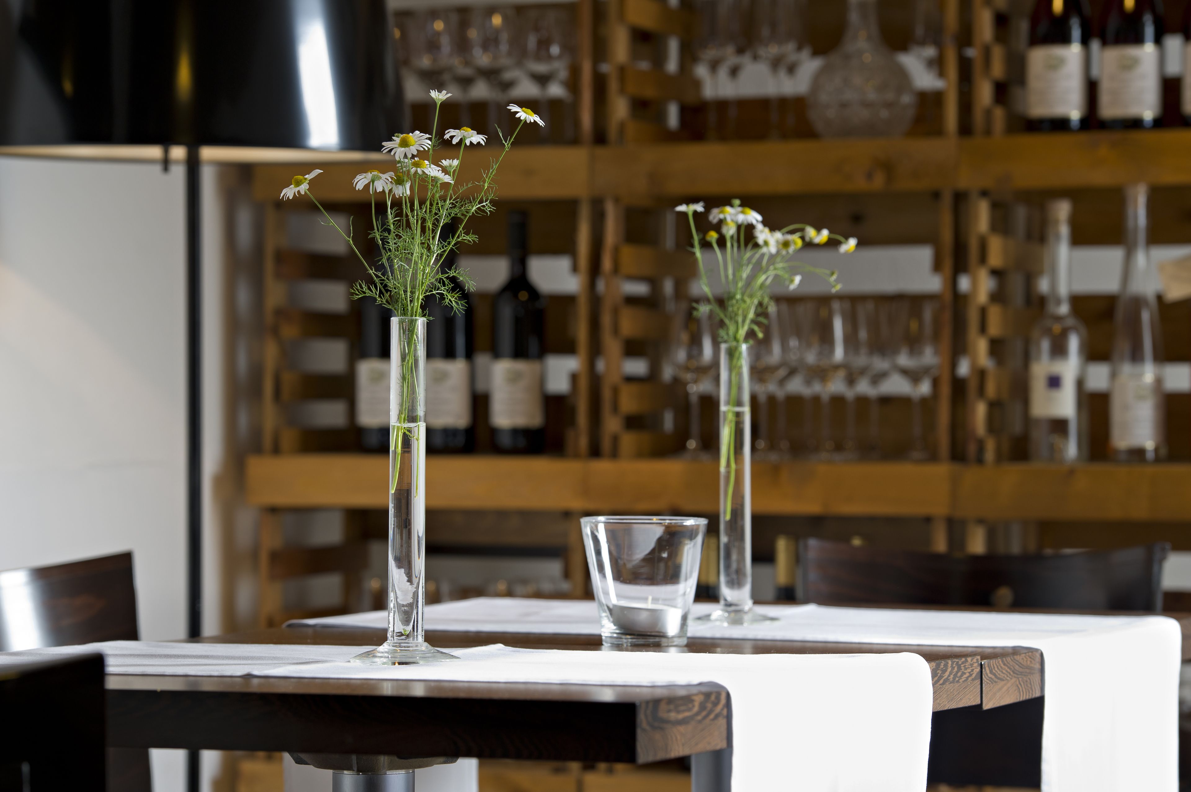 Uma mesa de restaurante com dois vasos de vidro contendo flores e um copo.