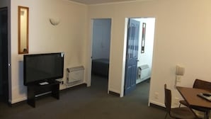 A room with a television on a stand, a bed, a door leading to another room, and a table with chairs. - 83 By the Sea Motor Lodge  (Lower Hutt)