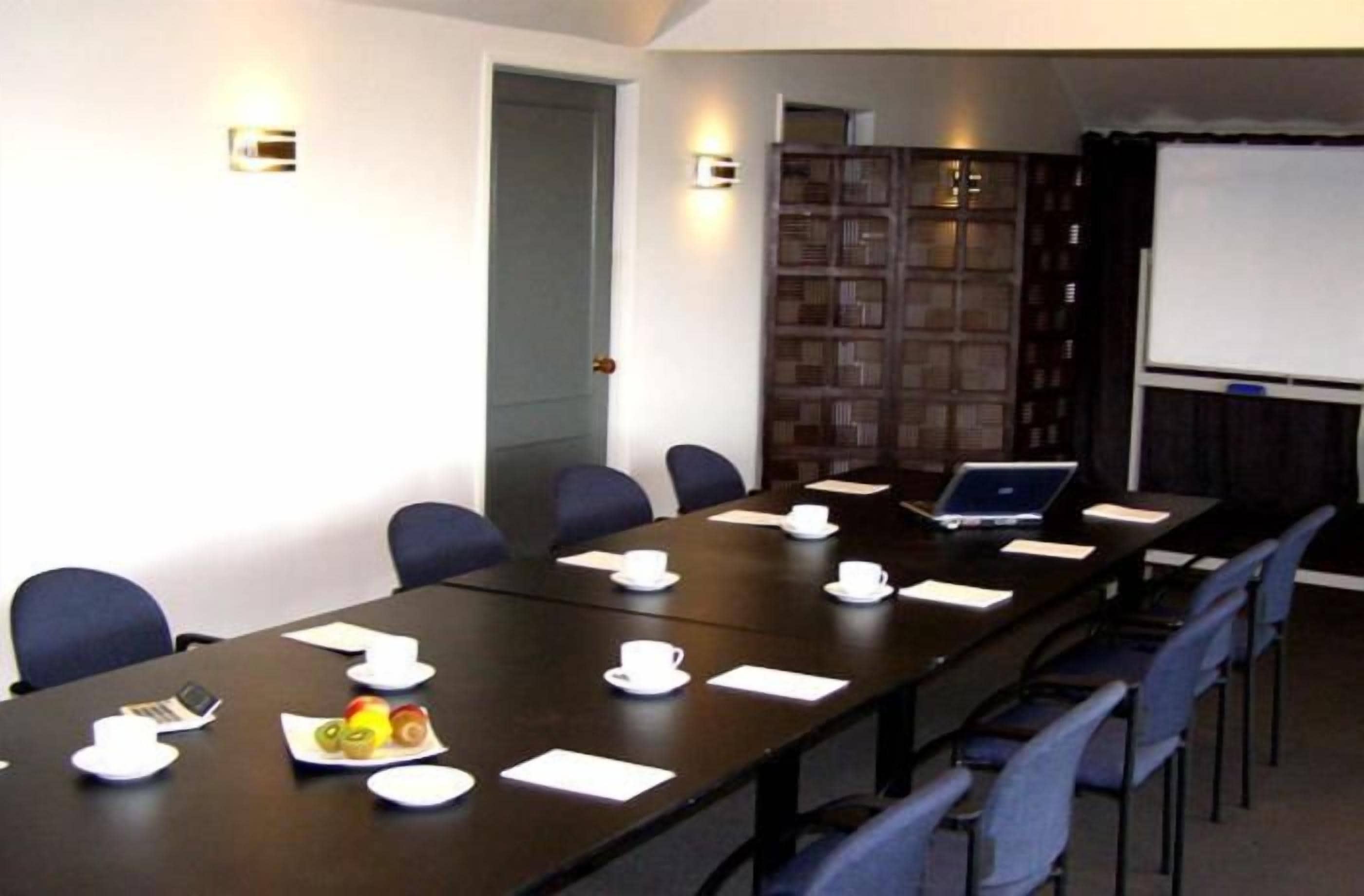 A conference room with a long table, chairs, a laptop, and a projector screen.