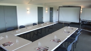 A conference room with long tables, chairs, a whiteboard, and a projector screen. - 83 By the Sea Motor Lodge  (Lower Hutt)