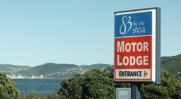 A sign for Motor Lodge with an entrance arrow, located near a scenic coastal area with hills and a body of water in the background.