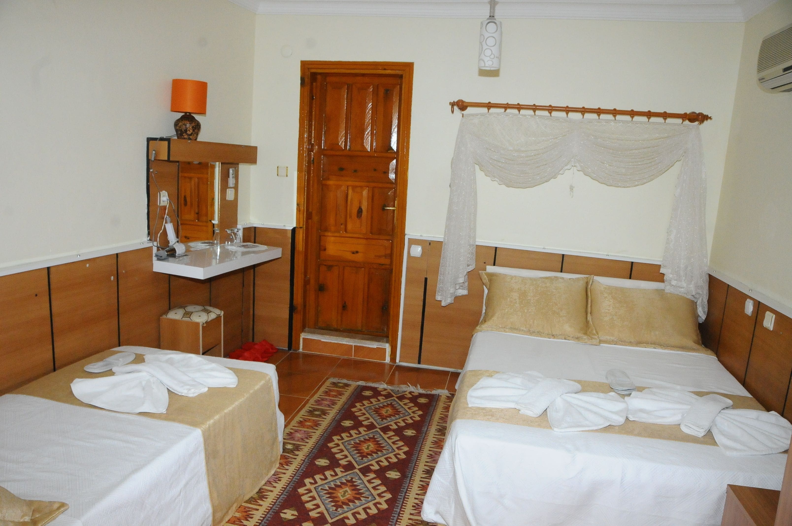A hotel room with two beds, a wooden wardrobe, a mirror, a sink, and a decorative rug.