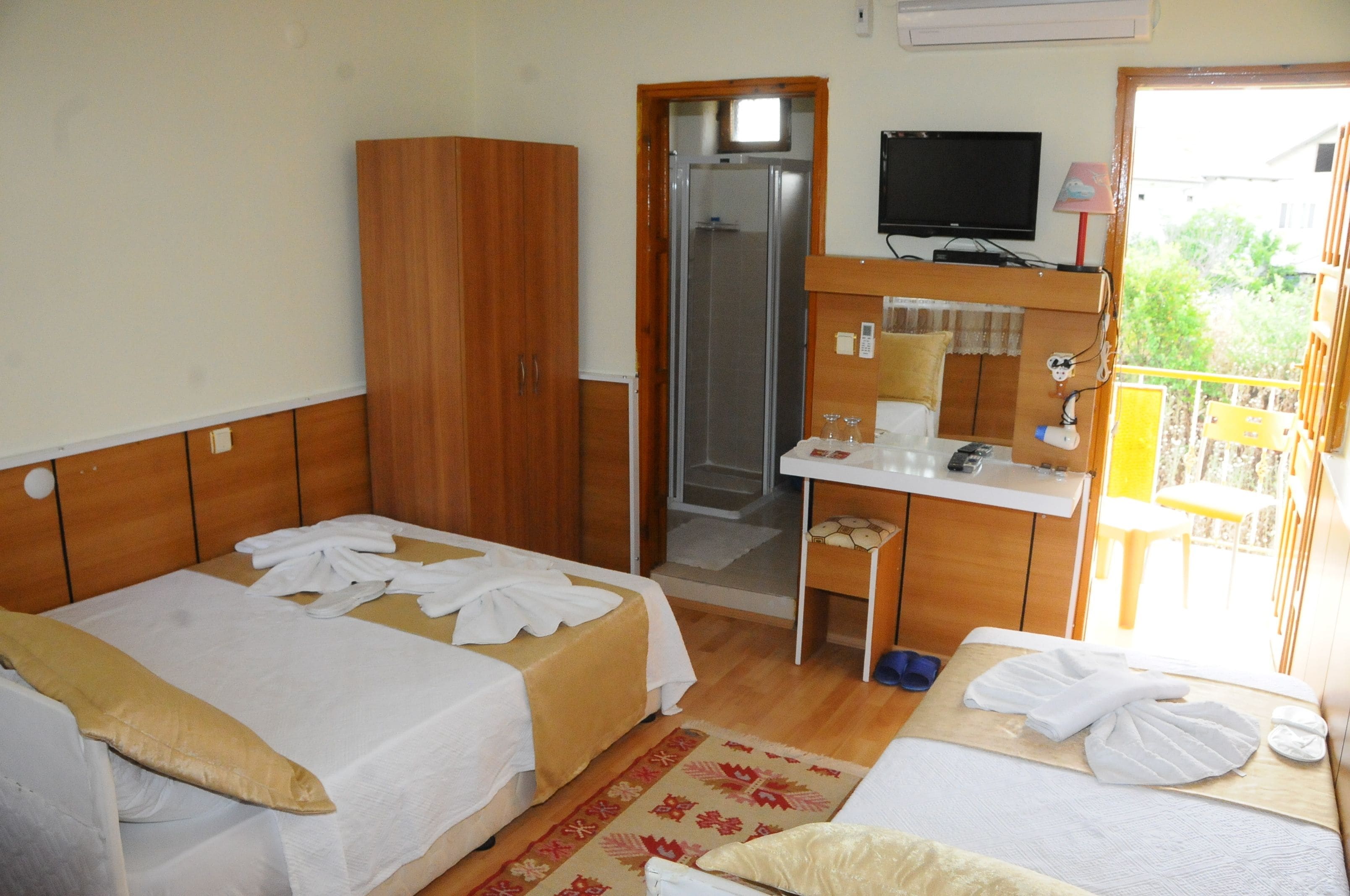 A hotel room with two beds, a desk, a mirror, a television, and a bathroom.