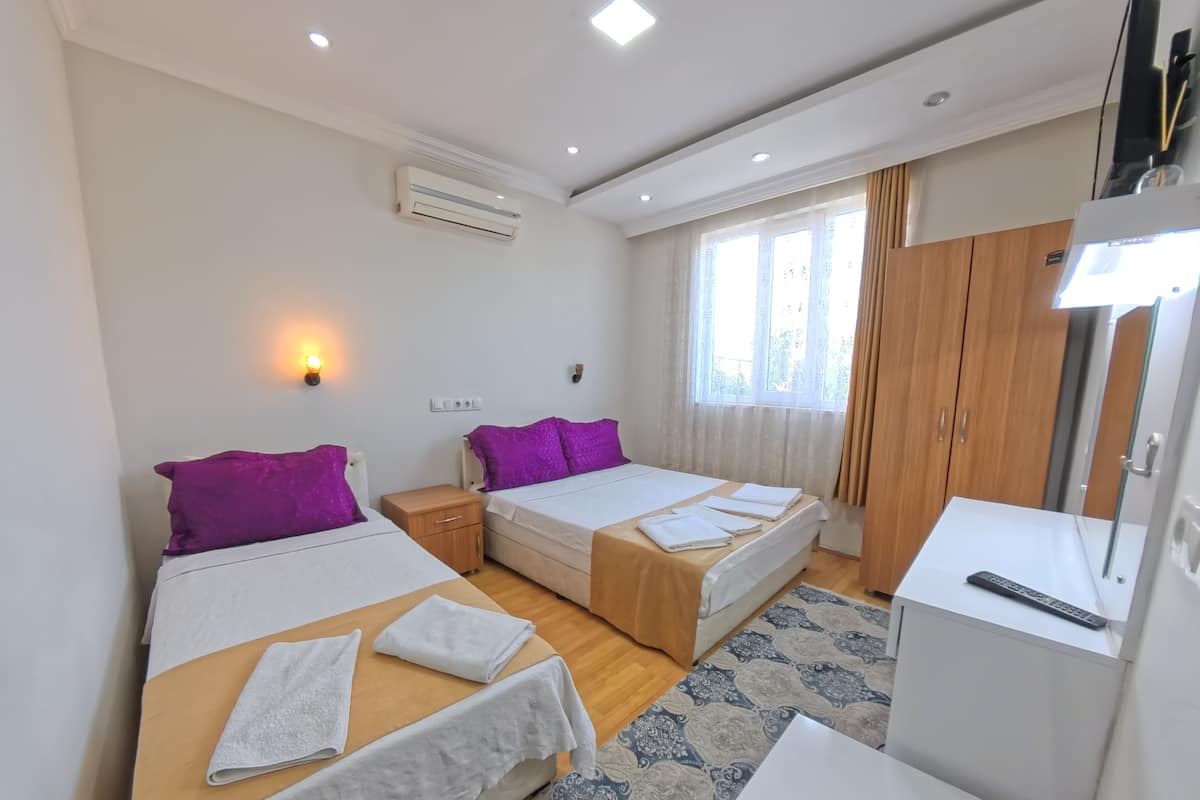 A hotel room with two beds, a desk, a TV, and a window with curtains.