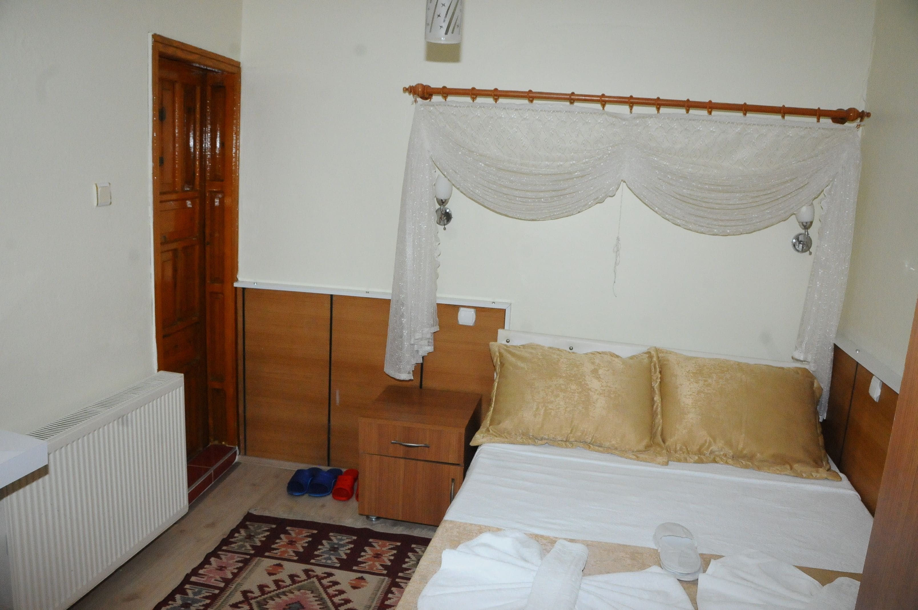 A bedroom with a bed, a nightstand, a wooden wardrobe, a radiator, and a door.