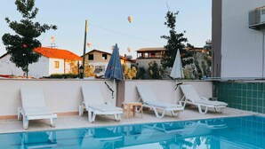 A swimming pool with lounge chairs and umbrellas, surrounded by buildings and trees. - Kervansaray Hotel & Pension (Denizli)