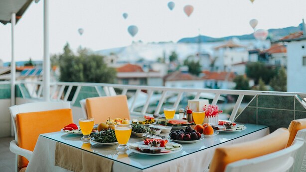 A table set with various dishes and drinks, overlooking a scenic view with buildings and hot air balloons in the distance. - Kervansaray Hotel & Pension (Denizli)