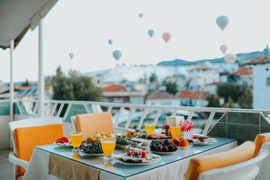 A table set with various dishes and drinks, overlooking a scenic view with buildings and hot air balloons in the distance. - Kervansaray Hotel & Pension (Denizli)