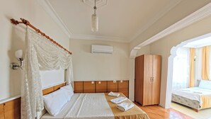 A hotel room with a bed, a wooden wardrobe, a nightstand, a bedside table, and an air conditioning unit. - Kervansaray Hotel & Pension (Denizli)