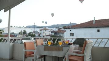 Une terrasse avec une table dressée pour deux personnes, d’où l’on peut admirer une ville aux bâtiments blancs et une montagne en arrière-plan.
