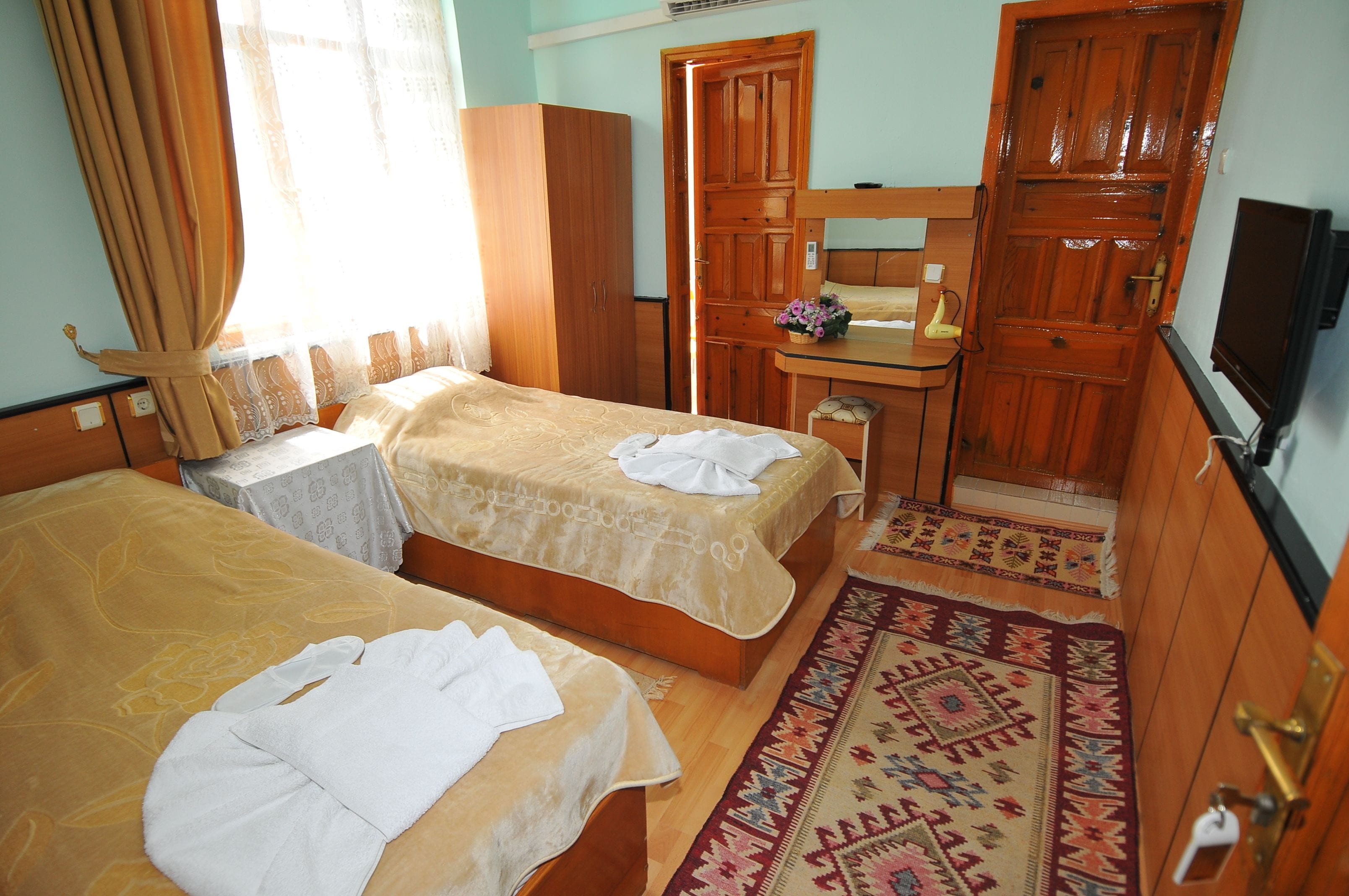 A hotel room with two beds, a wooden wardrobe, a small table with a mirror, and a TV on the wall.
