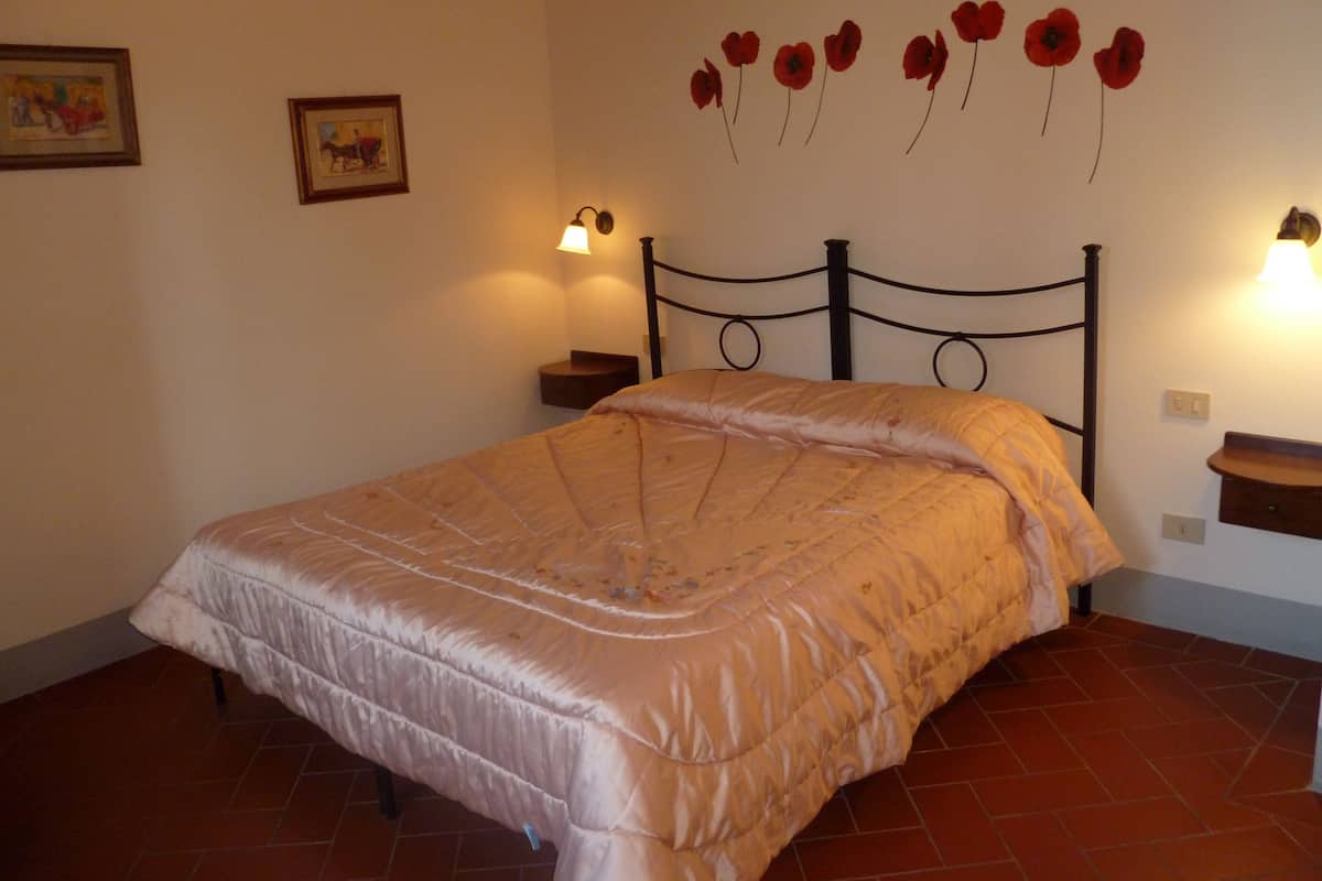 Un dormitorio con una cama, dos mesitas de noche, una lámpara de pared y una decoración floral roja en la pared.