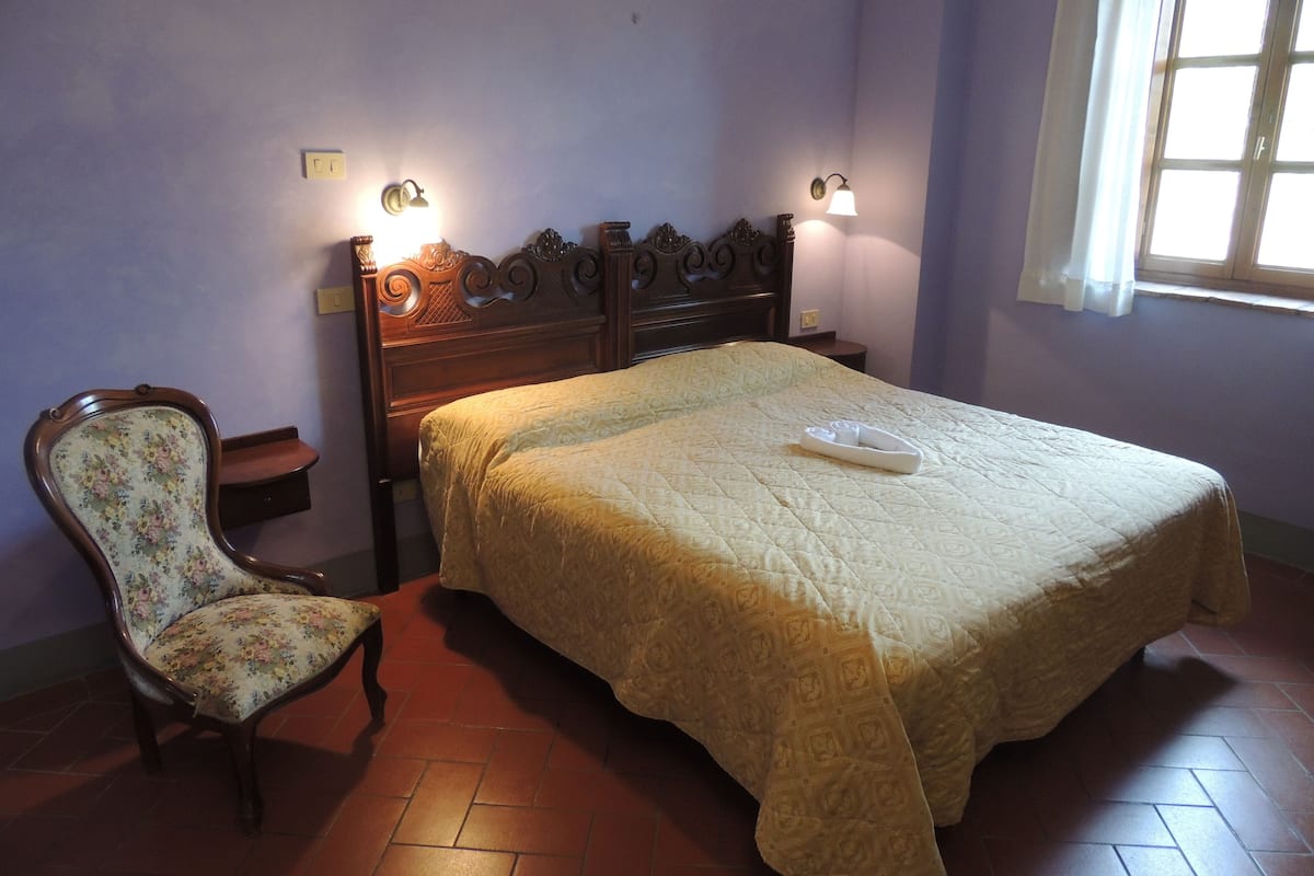 Un dormitorio con una cama de madera, un sillón floral y dos lámparas de pared.